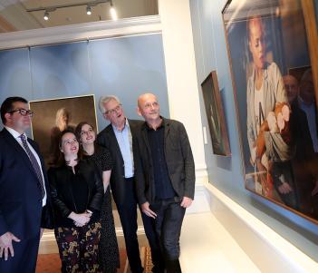 Photo of two women and three men looking at a portrait in a gallery