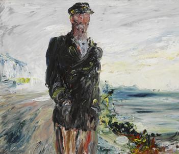 A man in a dark overcoat with his hands in his pockets, wearing a cap. In the background, the sea.  
