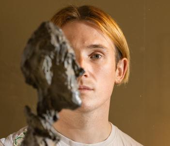 Richard Malone posing behind a bust by Alberto Giacometti