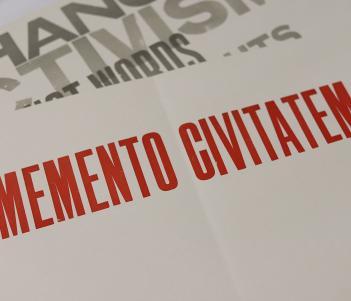 A sheet of paper with memento civitatem printed in red block capitals, with another sheet of paper visible beneath with fragments of words including activism and change