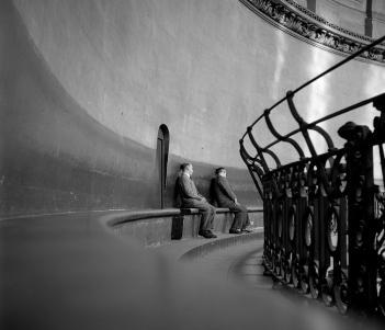 Black and white photograph of two men sitting on a bench within the curved dome of St Paul's Cathedral