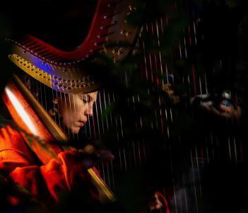 A woman plays the harp, her face visible through the strings.