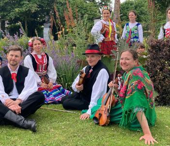 A group of musicians in colourful clothing sit in a park