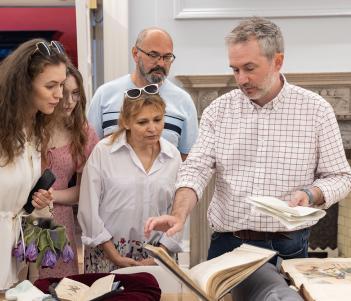 A group of people are gathered around looking at a rare book on display