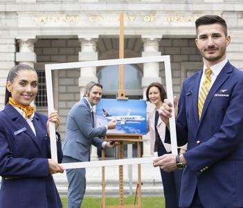 Two Ryanair flight attendants holding a blank picture frame with two people holding a picture of a Ryanair airplane in the background.