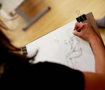 Photo of a woman drawing a human figure on paper.