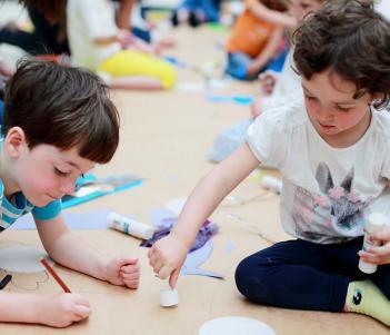 Photo of two children drawing on a giant sheet of brown paper on the floor.