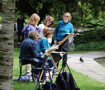 Photo of a group of five women painting at at easel outdoors.