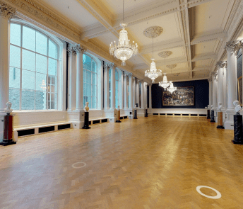 A long Gallery with chandeliers, polished wooden floors, and large windows at one side.