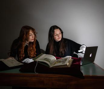 Two researchers looking at a laptop with rare books lying on the table on cushions