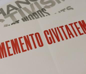 A sheet of paper with memento civitatem printed in red block capitals, with another sheet of paper visible beneath with fragments of words including activism and change