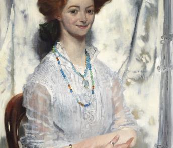 A woman with vibrart red hair in an updo smiles at the viewer. She wears a white dress and has flowers on her lap. Around her neck she has beaded necklaces, and has rings on her fingers. 